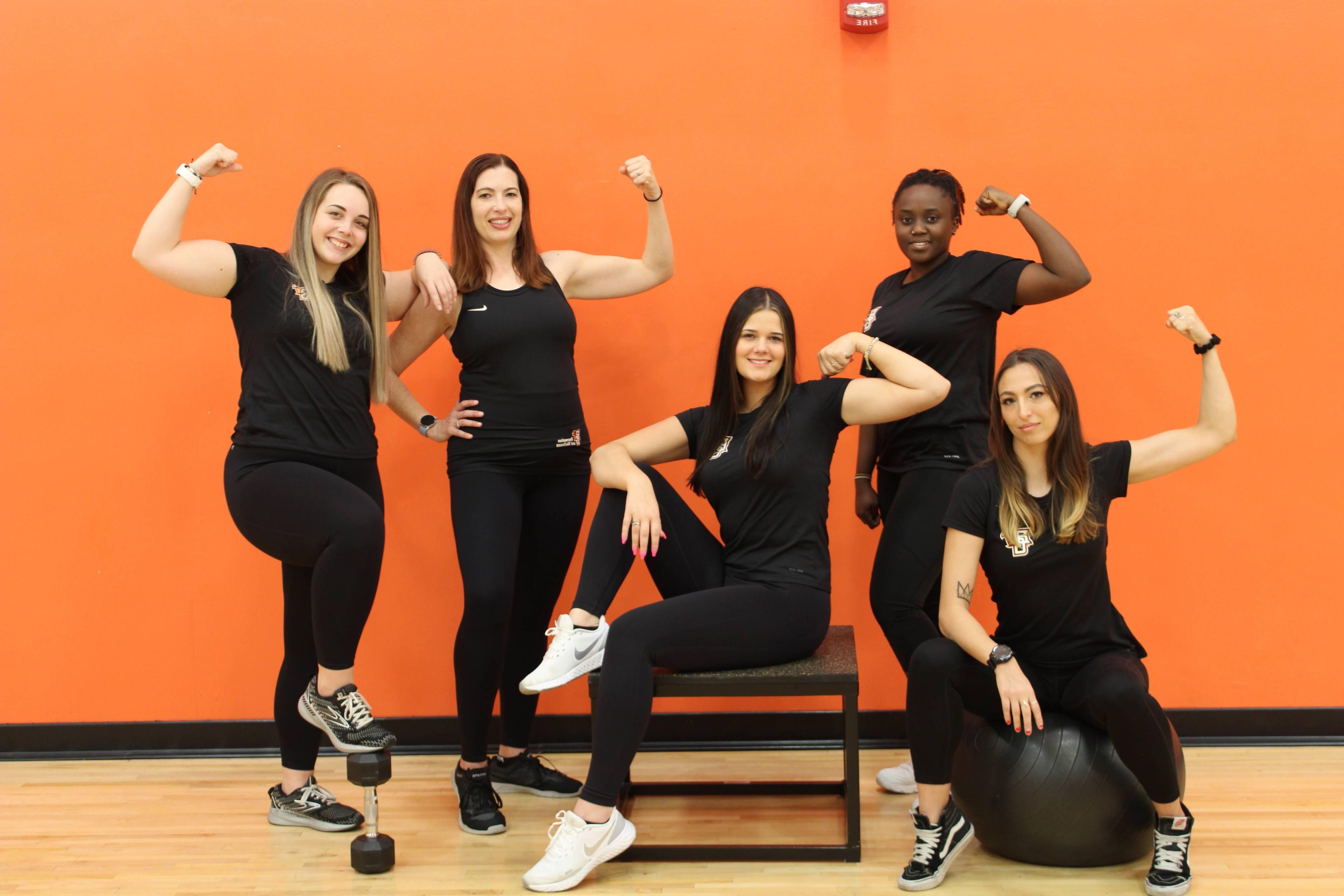 5 trainers posing with arms held high wearing black fitness staff apparel
